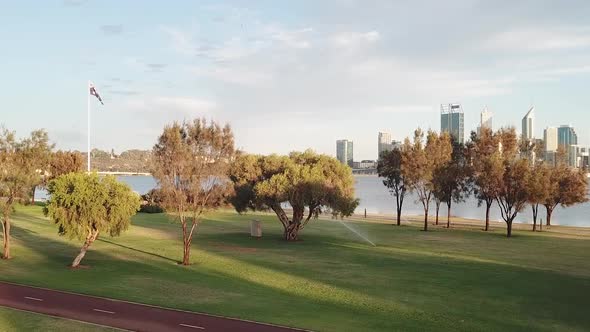 Australian flag pole in park, aerial pedestal up to reveal city in distance. Perth, Australia alt