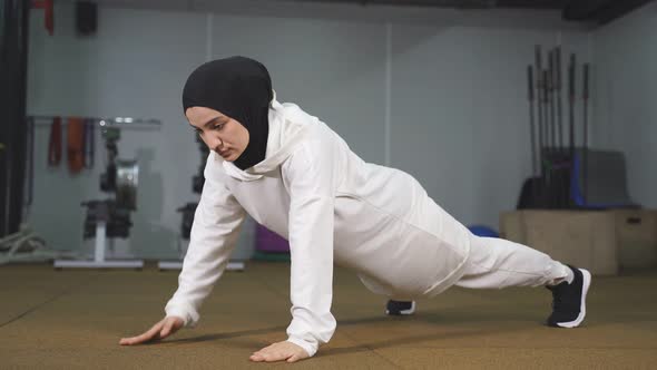 Muslim Woman in a Sports Hijab Does Exercises Planks Pushups in an Indoor Gym