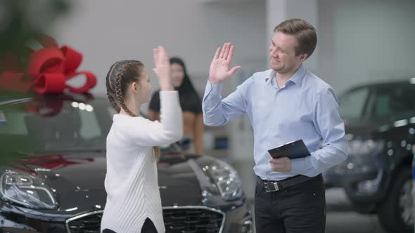 Cheerful Car Dealer and Joyful Little Girl Giving High Five in Slow Motion in Car Dealership alt