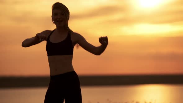 Silhouette of Young Beautiful Girl Dancing Zumba in Field at Sunrise alt