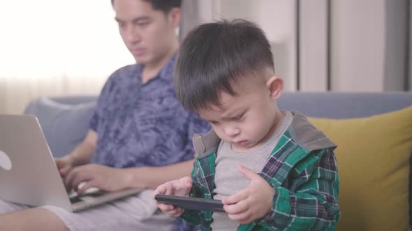Boring Boy Using Smartphone While Father Working On Laptop alt