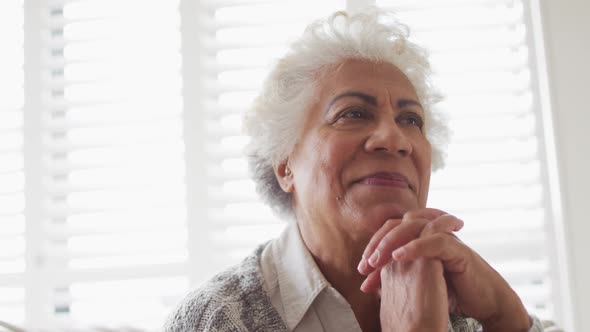 Close up of african american senior woman with hand on chin smiling at home alt