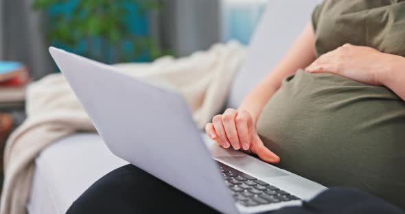 A Woman Dressed in Comfortable Clothes Relaxes on a Couch with a Laptop on Lap alt