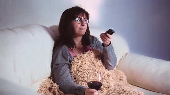 Brunette Woman Relax at Home with a Glass of Wine on the Sofa and Watches Tv in the Evening Listens