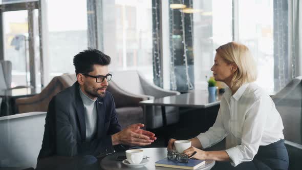 Businessman Talking To Attractive Mature Woman Coworker in Cafe at Table alt