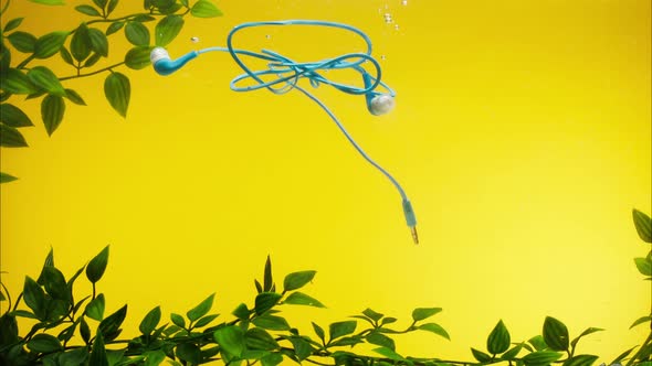 Sinking Blue Headphones in Water on Yellow Background Closeup Throwing Wired Earphones Into a River alt