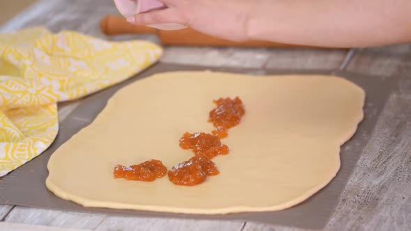 Spread the apricot jam on top of the dough on the kitchen table with a spoon.