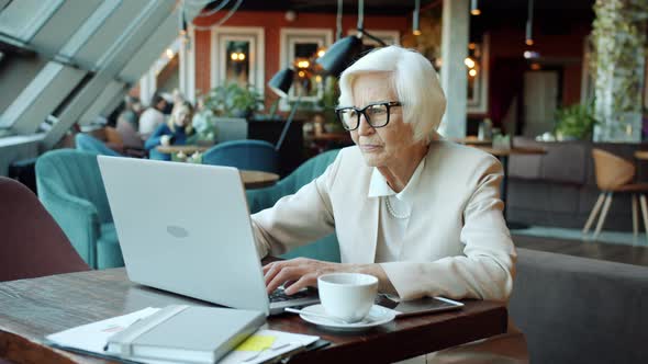 Portrait of Senior Businesswoman Working with Laptop Typing at Table in Cafe alt