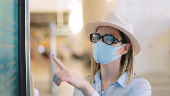 Traveler in Blue Face Mask Checking Flights on Timetable Screen in Empty Airport alt