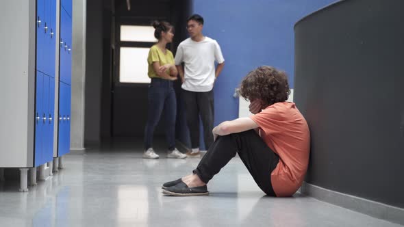 Sad Teenager Sitting Alone on Floor Victim of Bullying While Classmates Ignore Him alt