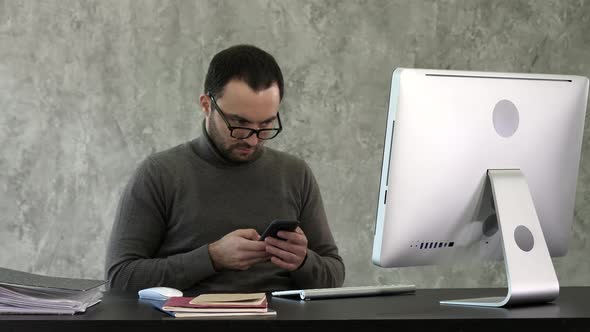 Bearded Young Businessman Working at Modern Office. Man Looking in His Smartphone and Typing alt