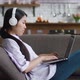 Asian Woman in Headphones Working with Laptop Computer Looking at Screen Typing Message Resting on - VideoHive Item for Sale