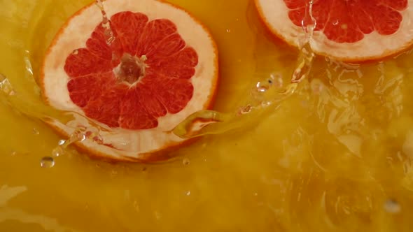 Grapefruit slices fall into the water on an orange background. Slow motion. alt