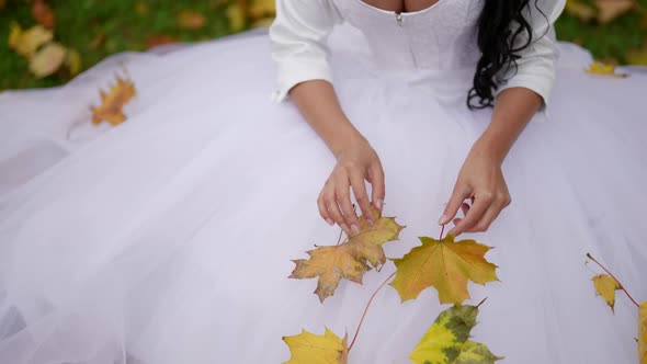 Bride in Autumn Beautiful Woman in Wedding Dress is Sitting on Ground in Park in Fall Day alt
