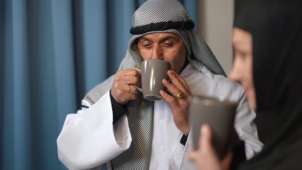 Portrait of Middle Eastern Husband Enjoying Taste of Morning Coffee Talking with Wife Smiling alt