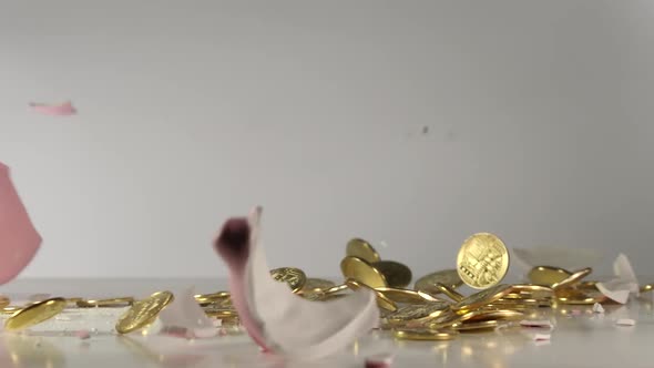 Pink pig money box with many golden coins falls on a table and breaks
