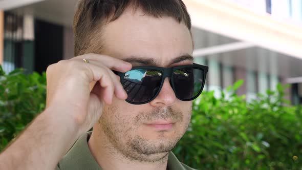 Man Looking at Camera From Under Black Sunglasses Showing Eye with Inflammation alt