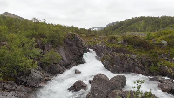 Glacial meltwater cascading down valley gorge waterfall, aerial view alt