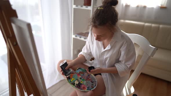 Beautiful Girl Artist Squeezes Paints Onto a Palette Getting Ready To Paint on Canvas alt