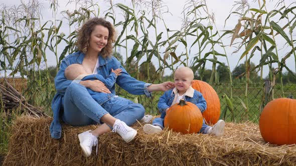 Young Mother Breastfeeding Her One Baby, Another One Is Sitting Right Next To Them on a Hay Bale in alt