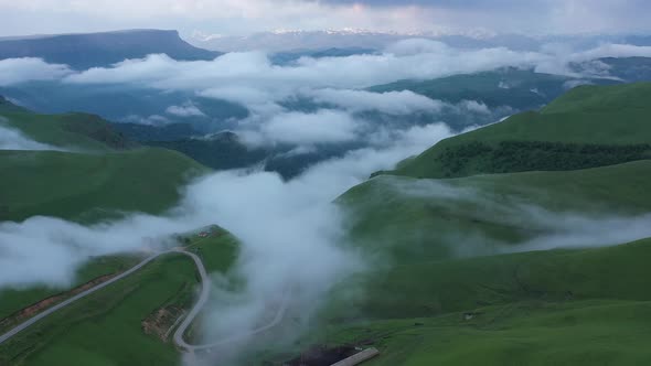 Drone Flight above green fields at the mountains in the clouds and fog.
