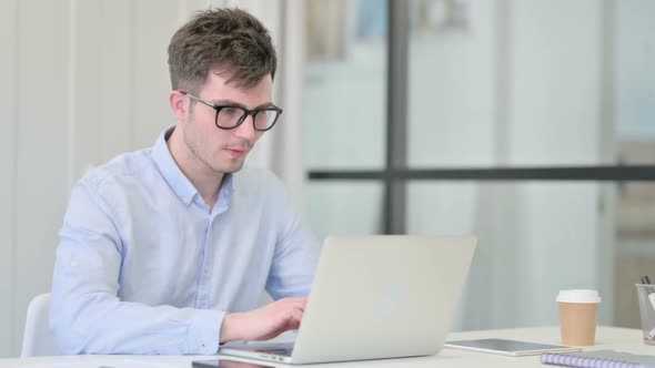 Attractive Young Man Looking at Camera While Using Laptop in Office alt