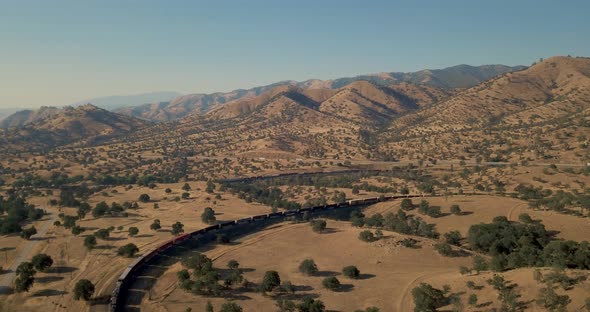 Long train moving slowly through Tehachapi Pass, California, golden hour, AERIAL alt
