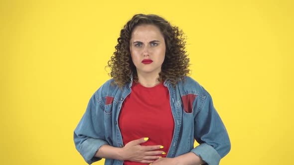 Cute Female Feels Very Bad, Her Stomach Hurts on Yellow Background at Studio, Slow Motion alt