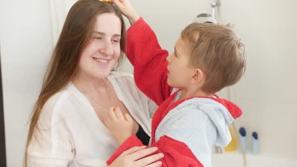 Slow Motion of Funny Smiling Mother and Little Son Drying and Combing Hair in Bathroom at Mirror alt