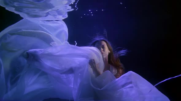 a Girl with Long Hair Slowly Sinks with Her Eyes Closed Into a Cloud of White Cloth in the Darkness alt
