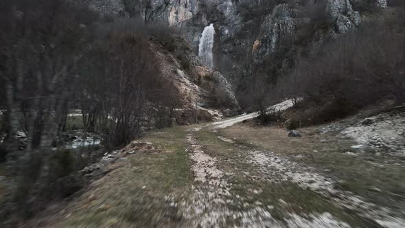 Drone flying fast through a path towards the Skakavic waterfall in Albania. alt