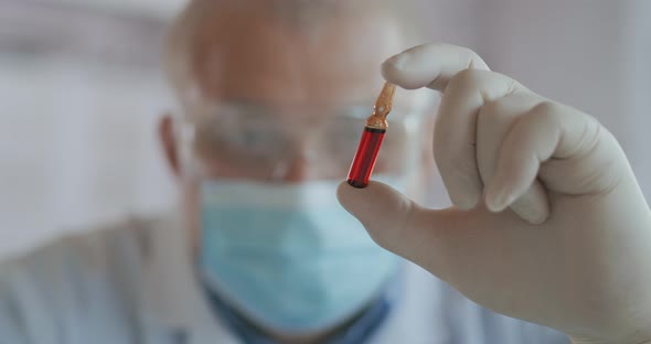 A Male Scientist Holds a Red Glass Ampoule with a Vaccine and Looks at It Close-up Slow Motion alt