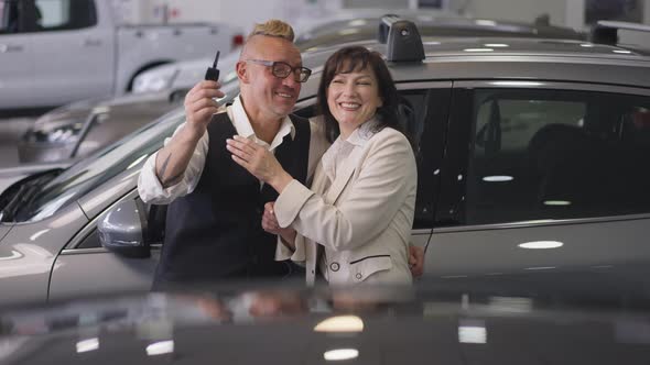 Excited Caucasian Wife Hugging Husband Bragging Car Key in Dealership in Slow Motion alt