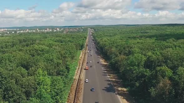 Long Straight Highway Through Dense Forest, Aerial Shot in Summer Day, Picturesque Clouds on Horizon