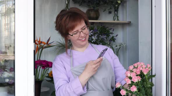 Female florist touching bouquet of roses and taking photo on smart phone for advertising