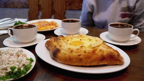 Adjarian Khachapuri on a Table in a Georgian Restaurant Next To Salad, Omelette and Coffee alt