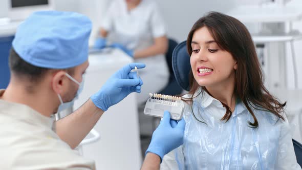 Male Dentist Choosing Teeth Enamel Shade Color Woman Patient Before Whitening Stomatology Procedure alt