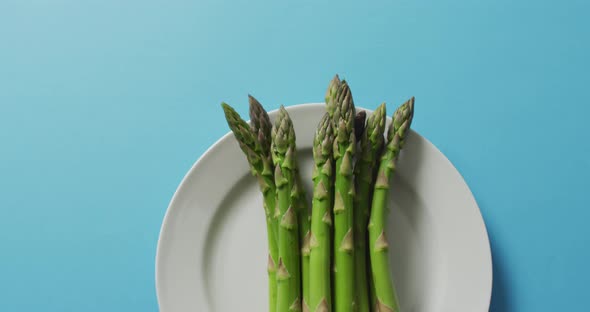 Video of fresh asparagus on white plate over blue background alt