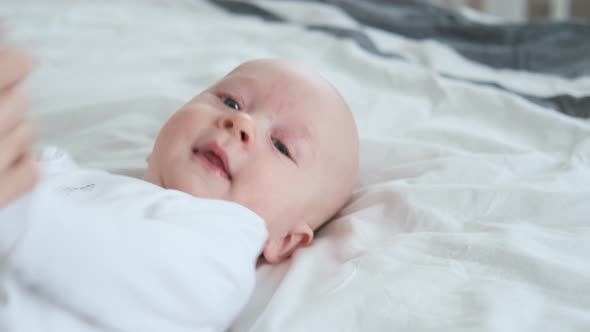 portrait of a toddler in white plays with mom while lying in bed