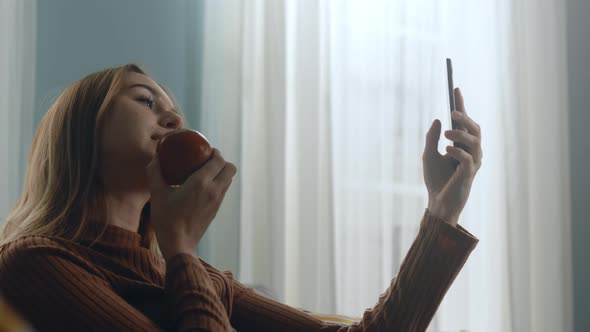 Beautiful Woman with a Red Apple Takes a Selfie on a Cell Phone alt