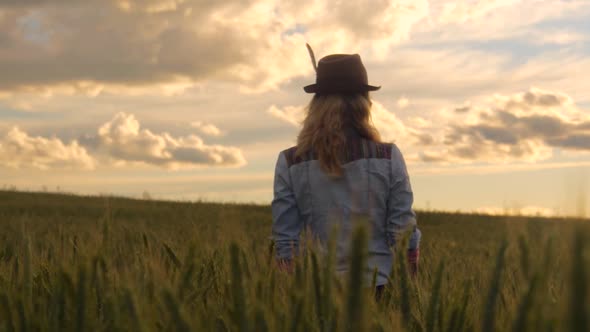 young caucasian bohemian female wearing hat in a  barley field during sunset