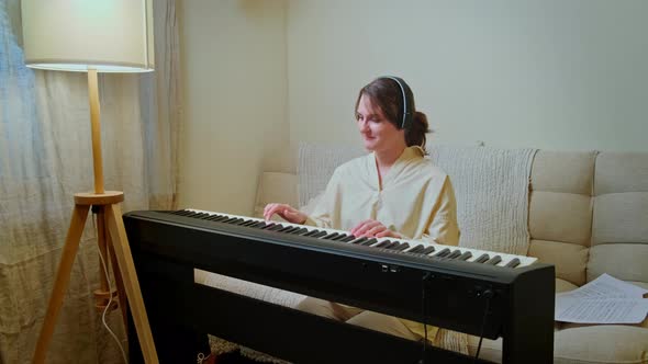 Woman musician playing electronic piano at home on sofa in living room