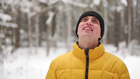 A Man in a Yellow Jacket Looks at the Snow in the Winter in the Woods and Smiles in Slow Motion alt