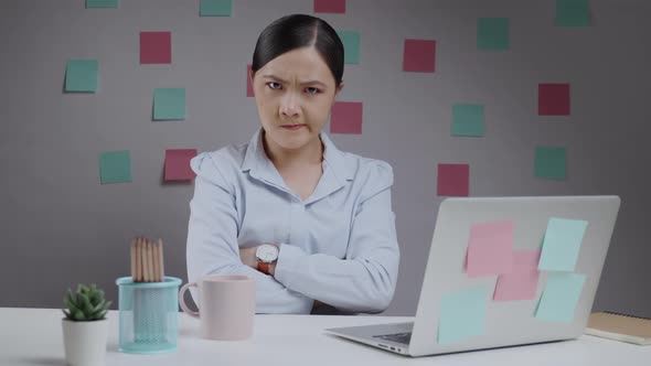 Asian woman working at home office looking at camera angry and arms crossed.