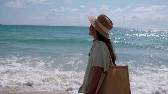 Slow motion of a beautiful young asian woman with hat and bag strolling on the beach