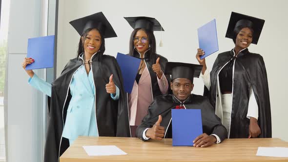 A Man is Sitting at a Desk and Three Women are Standing Behind Him and Showing Their Thumbs Up alt