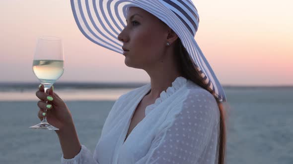 Elegant Woman with Glass of Wine Resting on Beach at Sunset