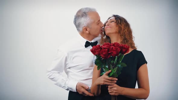 A Caring Middleaged Husband Gives a Bouquet of Scarlet Roses and a Gift in a Gift Box to a Beautiful