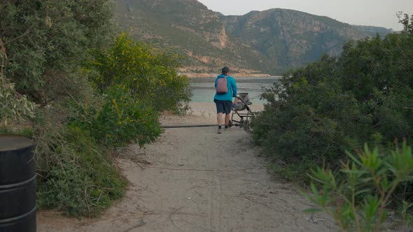 Father with Stroller Walks on Sandy Road to Beach Near Sea alt