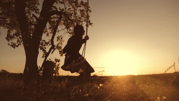 Silhouette Young Girl Swinging on a Swing Under a Tree in Sun. Family Fun in Nature. alt